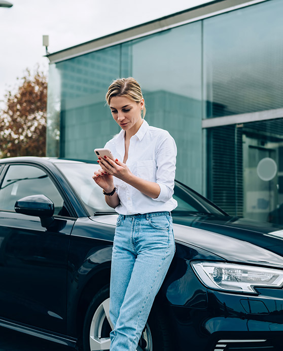 Woman in white shirt and jeans leaning on a car