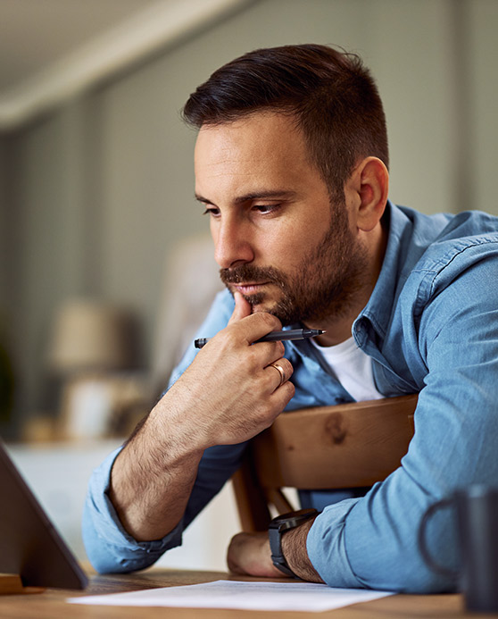 Man in blue shirt sitting in front of computer thinking