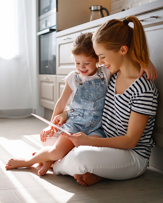Mother and her toddler girl sitting on the floor in their kitchen