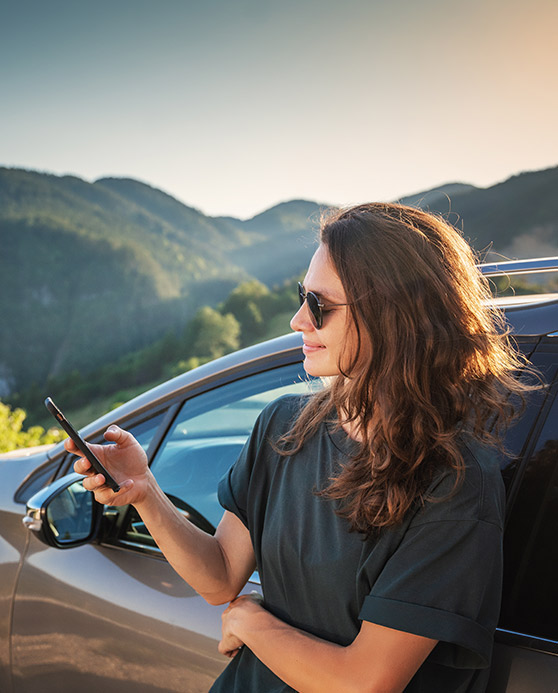 Woman leaning on her car while looking at her phone