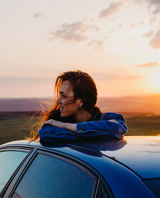 Woman leaning on car at sunset